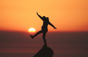 Person balancing on rock at sunset